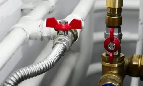 Close up of industrial gas line pipes with red shut off butterfly valves and flexible metallic connectors.